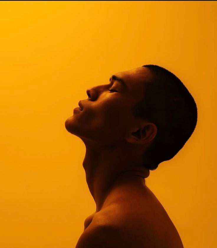 A man with his head tilted back and eyes closed in warm amber light