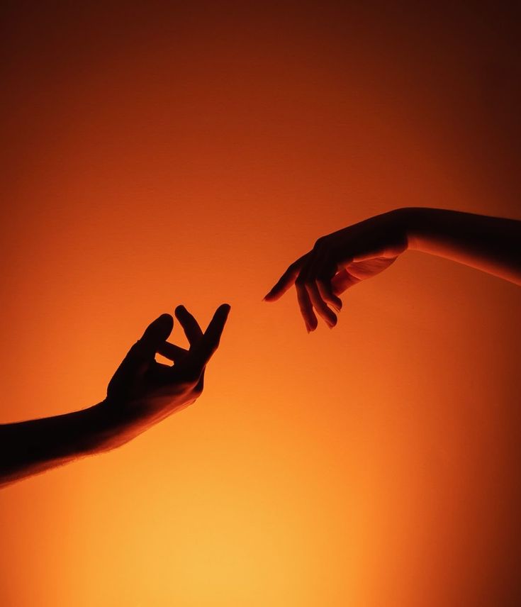 Two hands reaching towards each other against orange light